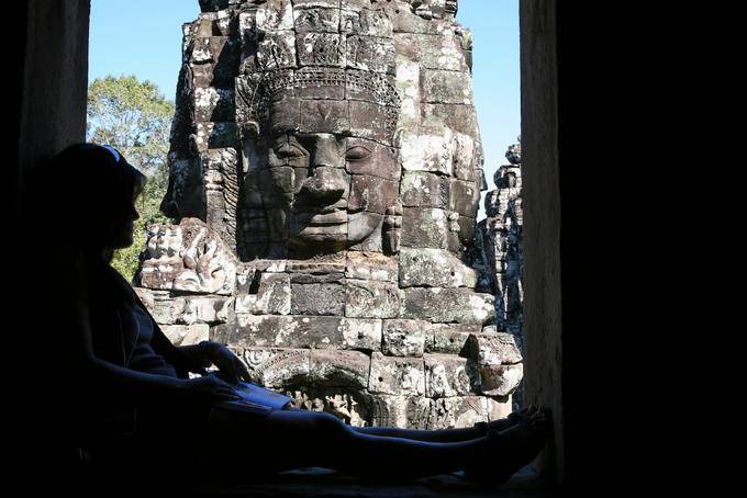 Leggendo all'ombra davanti alla faccia di pietra, Bayon, Angkor Thom, Angkor, Cambogia