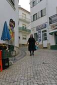 La donna in nero per la strada acciottolata, Nazaré, Portogallo.